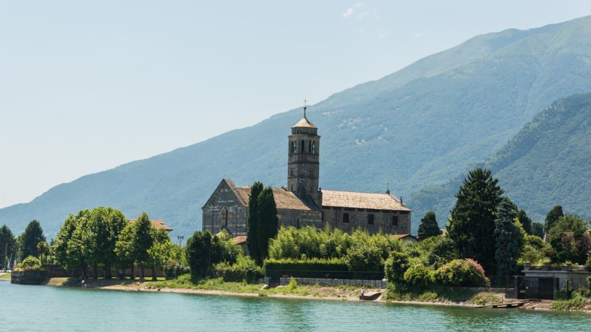 Scenic view of a historic church on Lake Como's shore in Lombardy, Italy, surrounded by lush greenery.