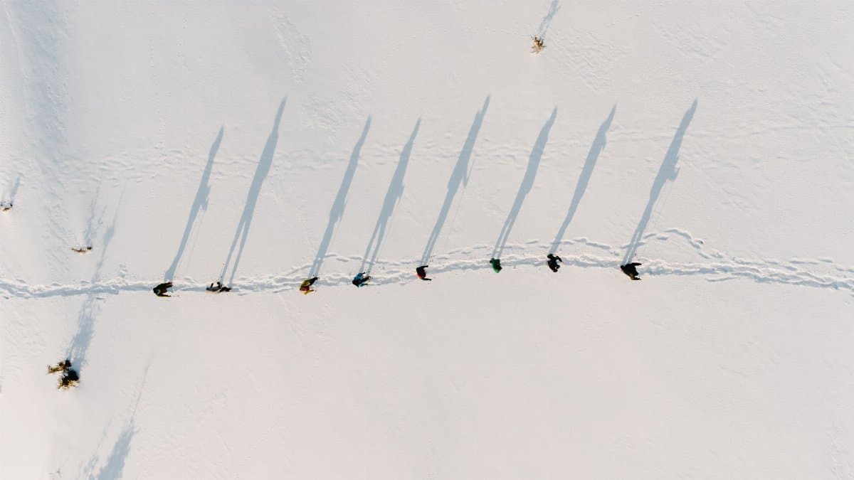 Drone captures people trudging through snow in Rakhivs'kyi district, creating long shadows over white landscape.
