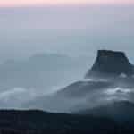 Serene view of Adam's Peak at dawn, shrouded in mist and gentle clouds, in Sri Lanka's lush landscape.