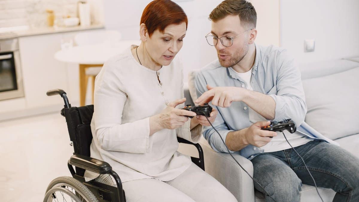 Older woman in wheelchair and young man play video games together, fostering connection.