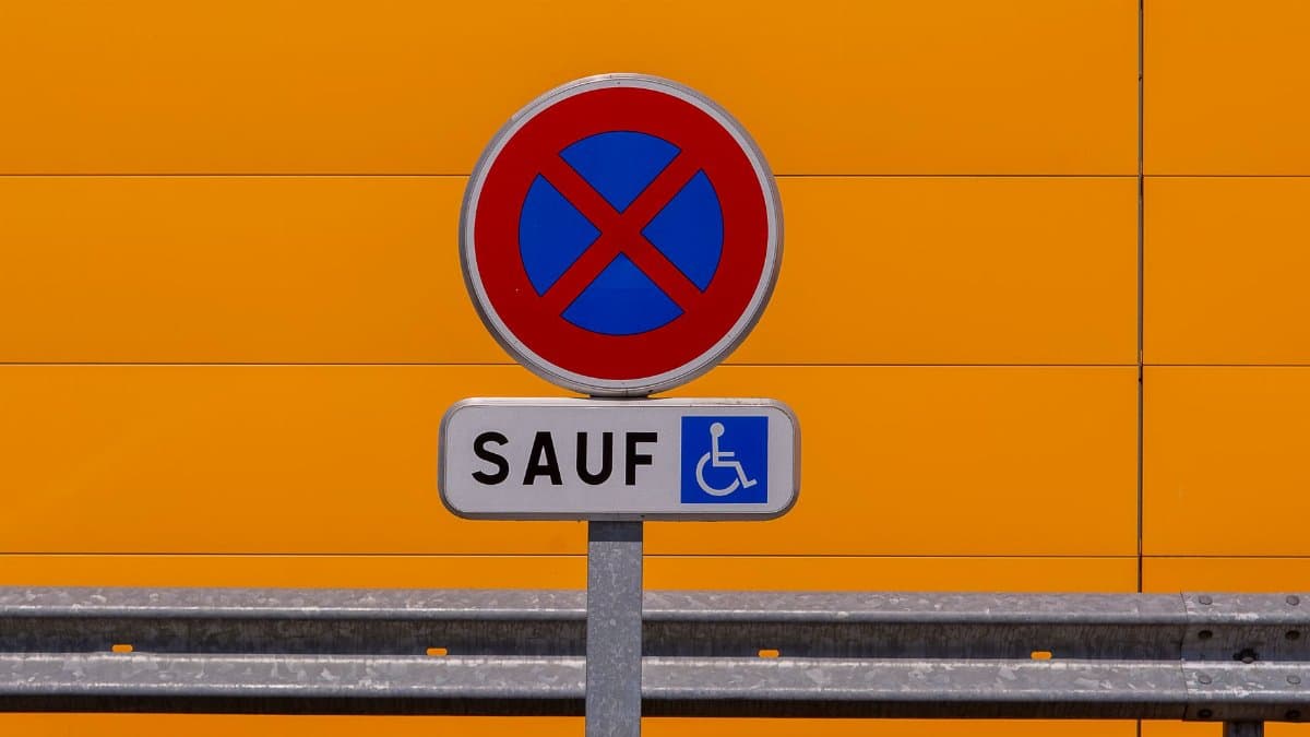 A traffic sign for disabled parking against a bright orange wall.