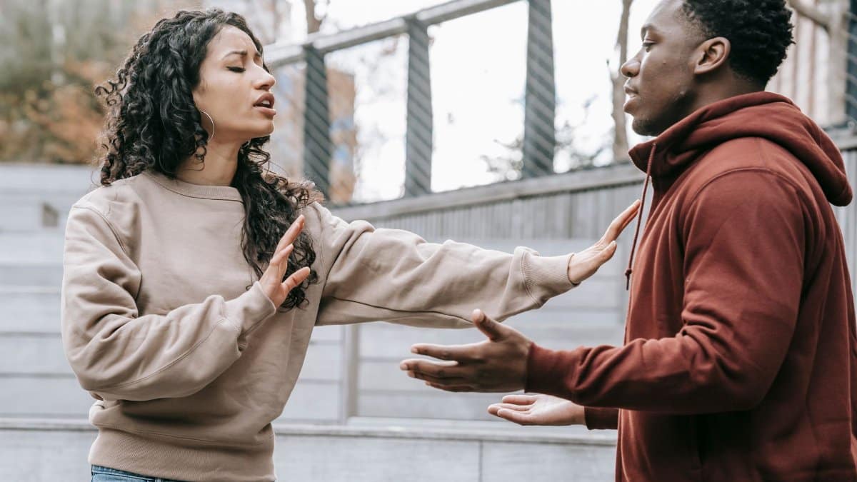 Side view of ethnic woman with outstretched arms trying to stop African American man while breaking up on street in city