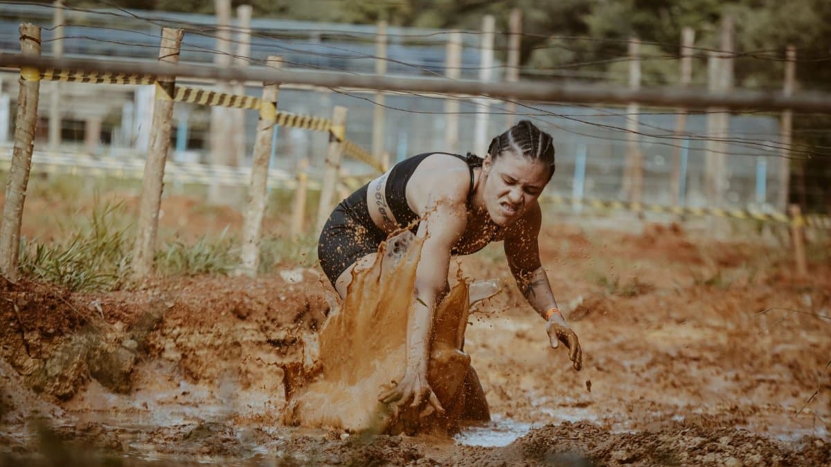 Female athlete tackling a muddy obstacle race, showcasing strength and determination outdoors.