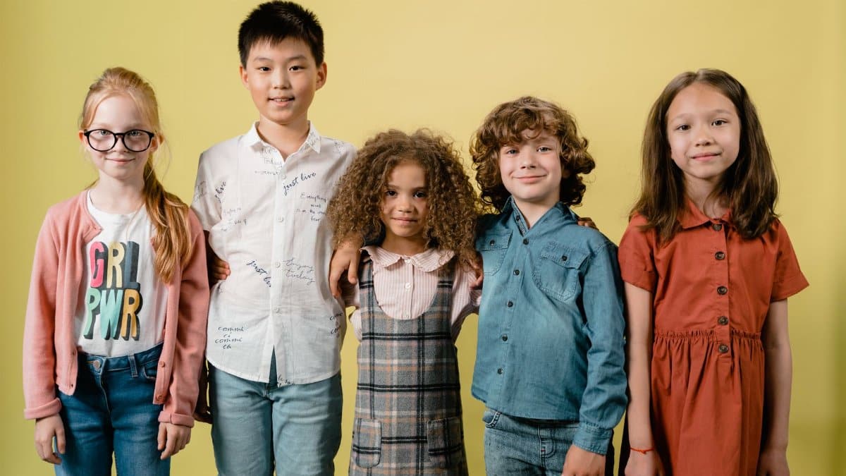Five diverse children smiling against a yellow background in a studio setting.
