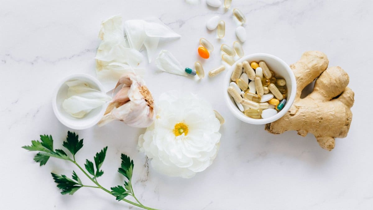 Top view of herbal medicine and supplements with ginger, flower, and capsules on a white background.