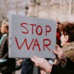 Crowd of people in a peaceful protest holding a 'Stop War' sign outdoors.
