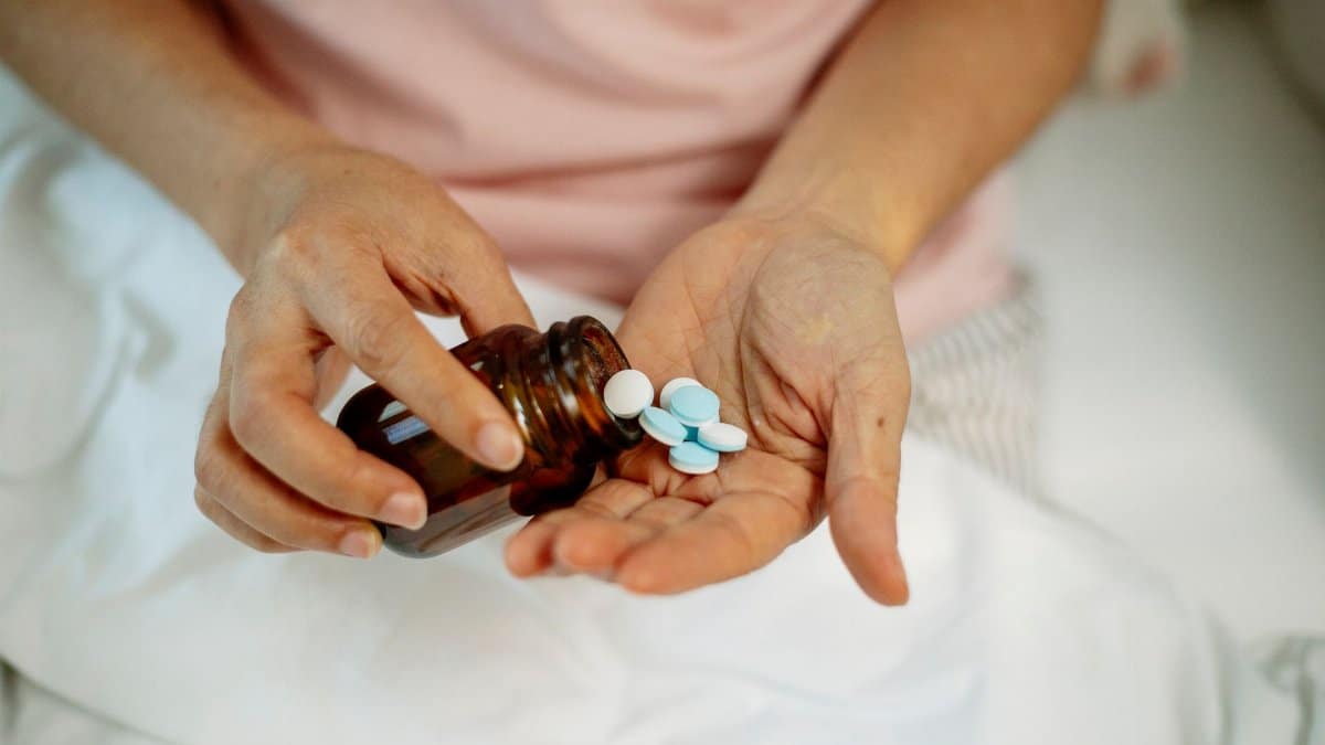 From above of crop anonymous female demonstrating round shaped pills in hand on blurred background