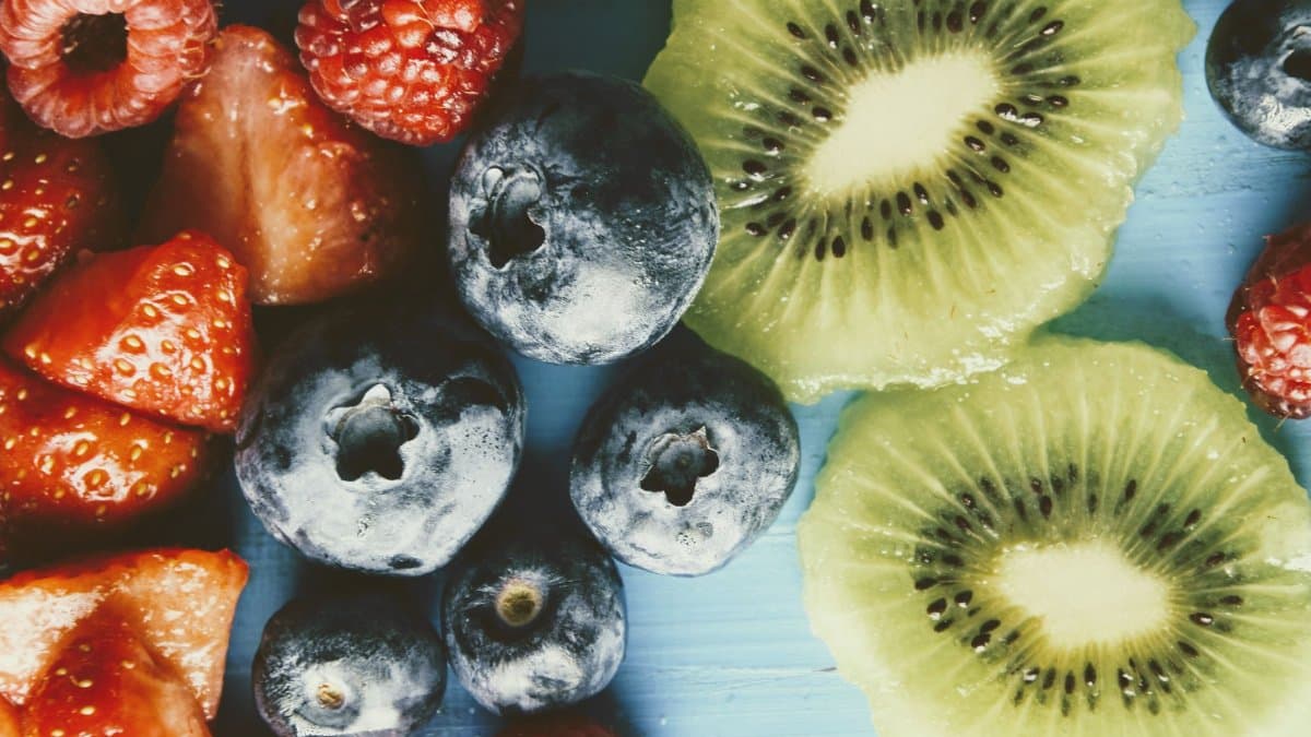 Close-up of fresh berries and kiwi slices on a blue background, showcasing vibrant colors.