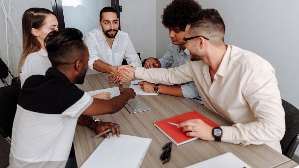 A diverse group of professionals collaborating in a modern office setting, shaking hands to signify teamwork.