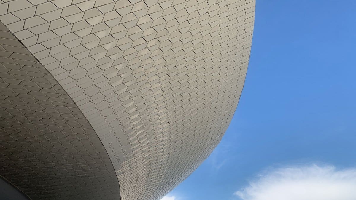 Curved architectural facade with hexagonal pattern set against a clear blue sky.