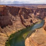 A stunning aerial view of the Colorado River winding through the Grand Canyon's majestic rock formations under a summer sky.