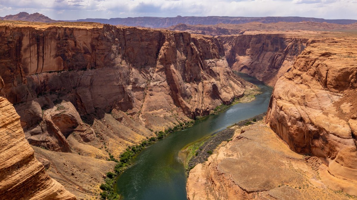 A stunning aerial view of the Colorado River winding through the Grand Canyon's majestic rock formations under a summer sky.