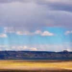 A scenic view of a vast field under a rainy sky in Page, Arizona, highlighting dramatic weather.