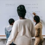 Back view of anonymous African American woman watching on pupils writing on whiteboard in classroom