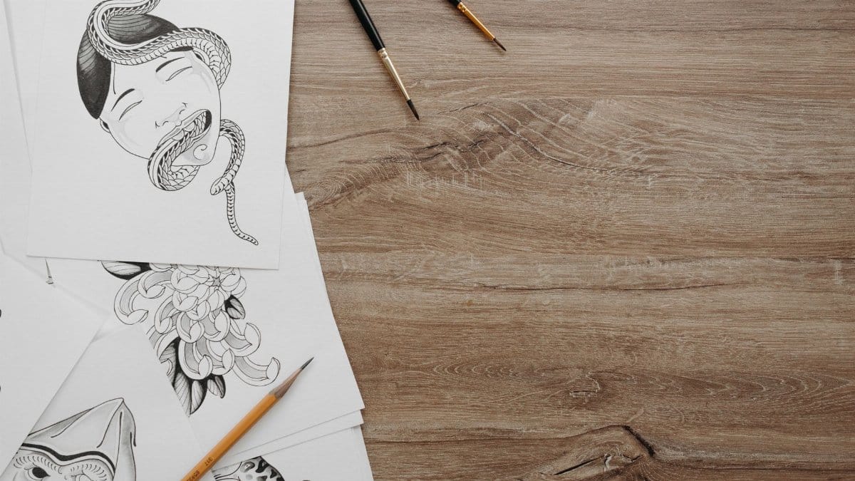 Creative sketches with brushes and pencil on a wooden table, showcasing artistic expression.