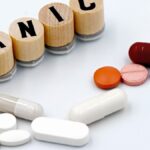Assorted pills arranged beside wooden tiles spelling 'PANIC', symbolizing anxiety treatment.