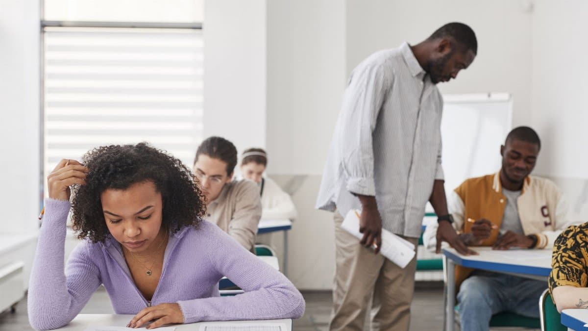 A diverse group of students taking an exam in a modern classroom with a teacher supervising.