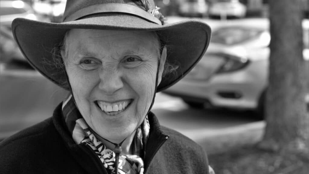 Black and white portrait of a smiling elderly woman wearing a hat, outdoors in Geneva, IL.