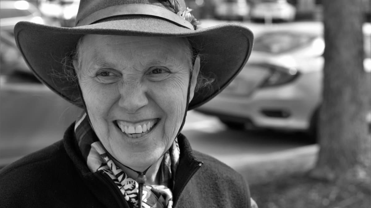 Black and white portrait of a smiling elderly woman wearing a hat, outdoors in Geneva, IL.