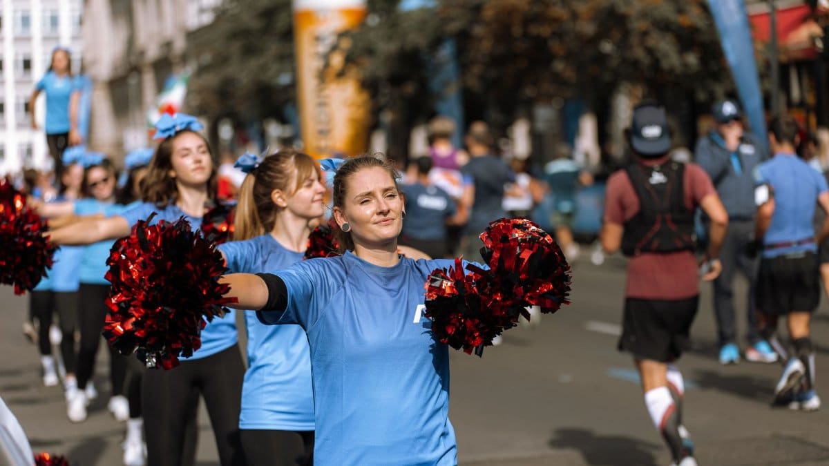 Cheerleaders in blue uniforms perform with red pom-poms at a street event.