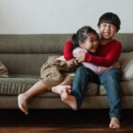 Two happy kids hugging and laughing while sitting on a couch in a cozy living room setting.
