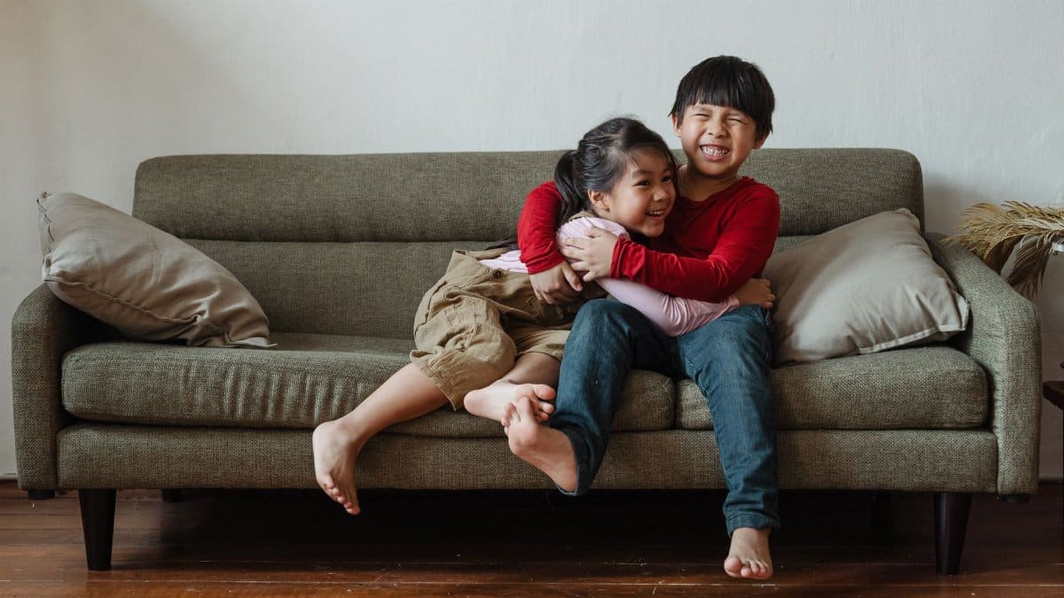 Two happy kids hugging and laughing while sitting on a couch in a cozy living room setting.