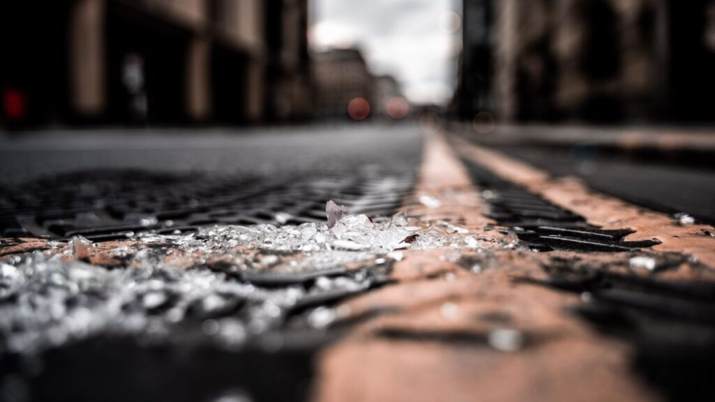 Close-up of broken glass pieces scattered on a city street with blurred buildings.