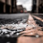 Close-up of broken glass pieces scattered on a city street with blurred buildings.