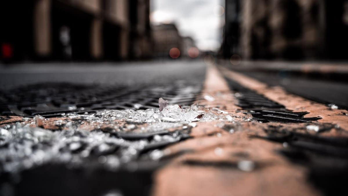 Close-up of broken glass pieces scattered on a city street with blurred buildings.