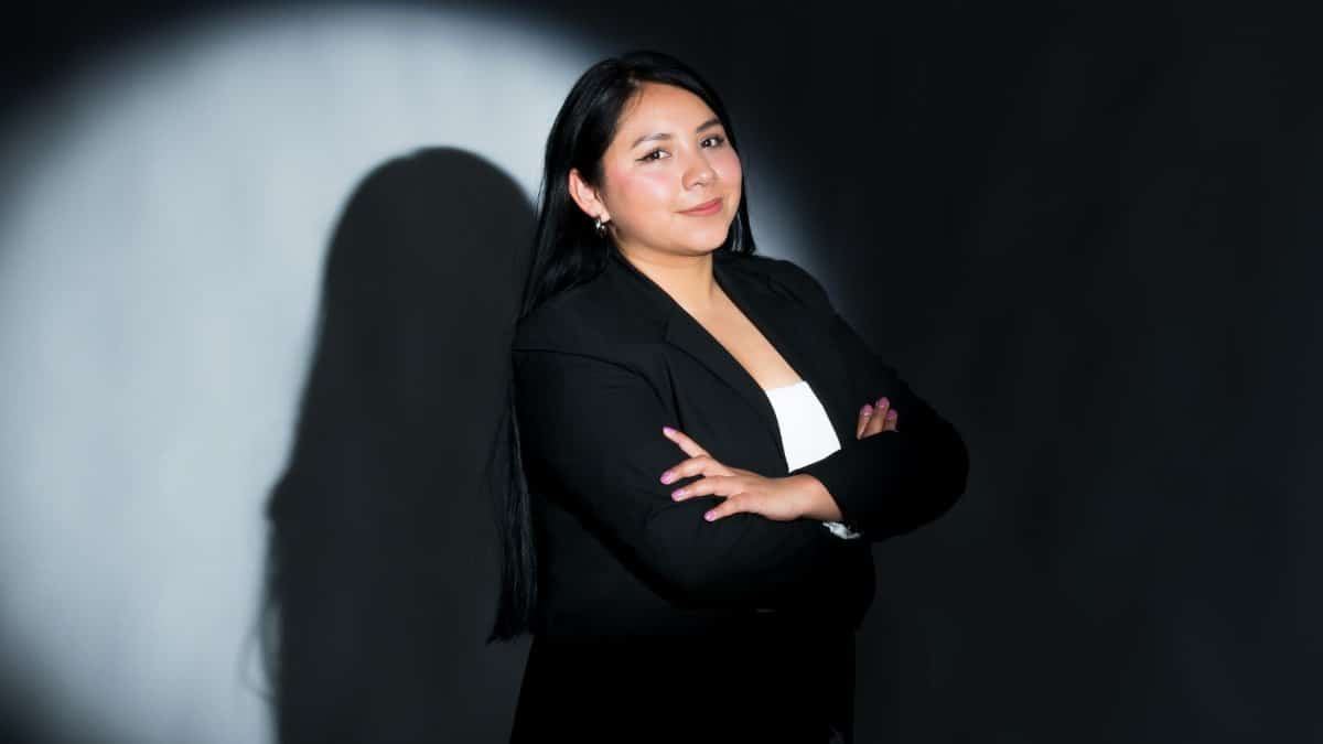 A professional portrait of a confident businesswoman in a black suit against a dark background.