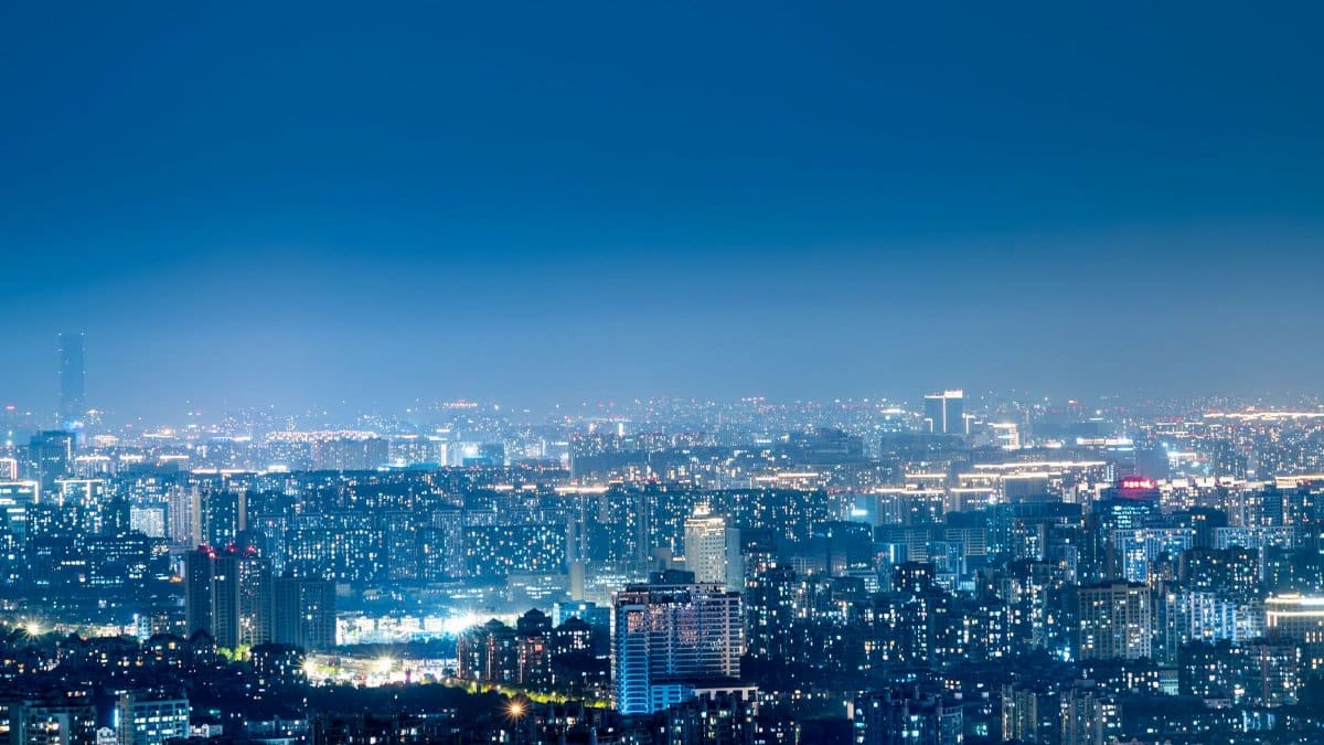 Panoramic view of a bustling city skyline illuminated at night, showcasing urban development and vibrant lights.