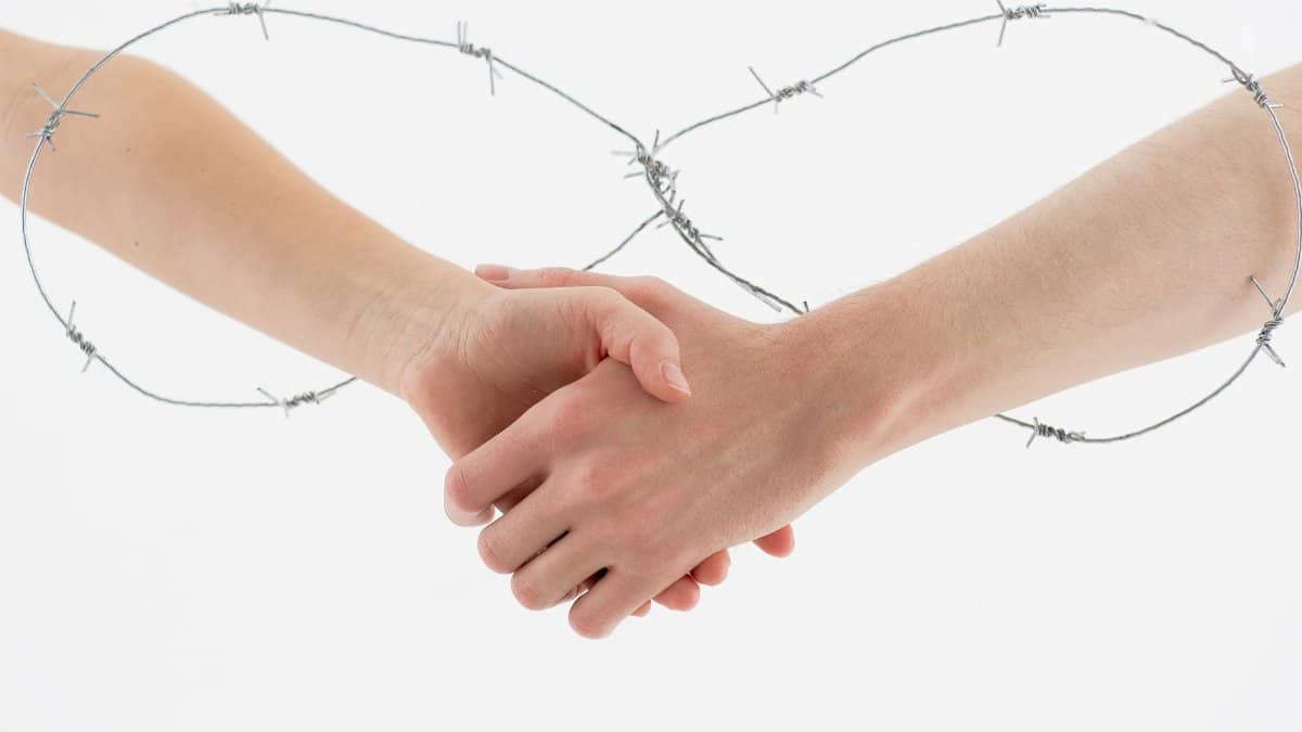 Symbolic handshake wrapped in barbed wire on a white background representing restriction and unity.