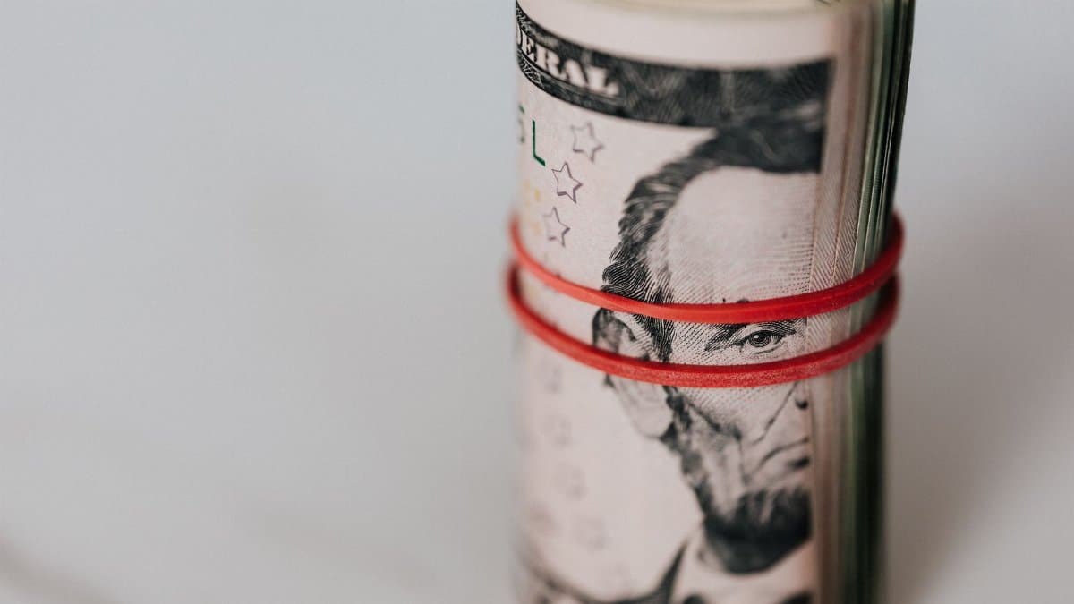 Pack of US five dollar banknotes twisted into roll and tightened with red band