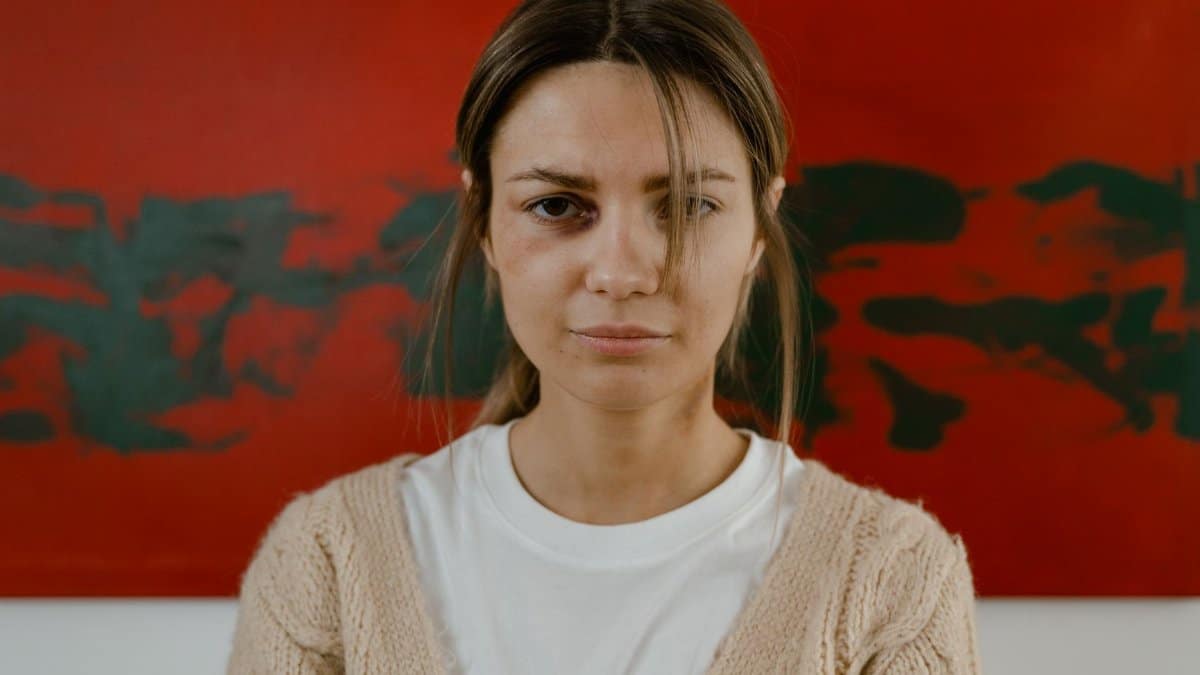 A woman stands pensively with a red abstract art background, expressing contemplation.