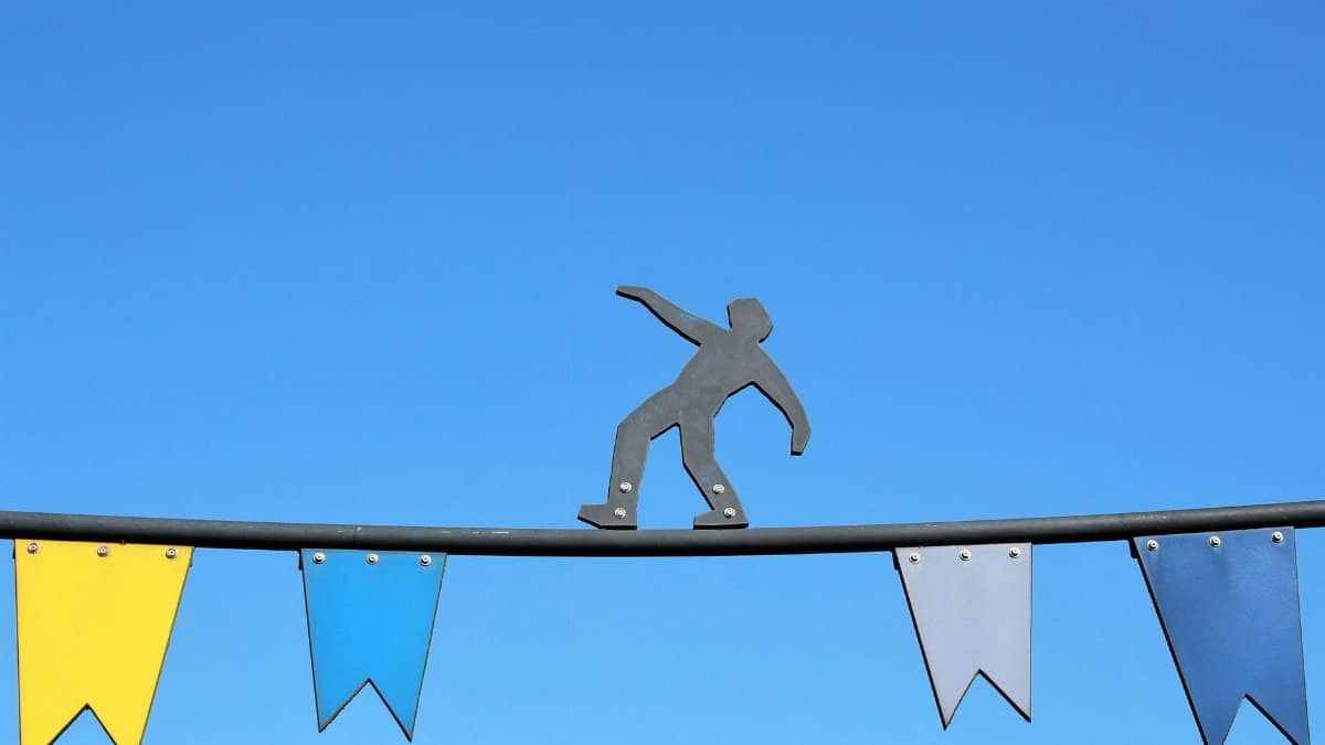 Metal figurine balancing on a wire against clear blue sky with colorful flags.