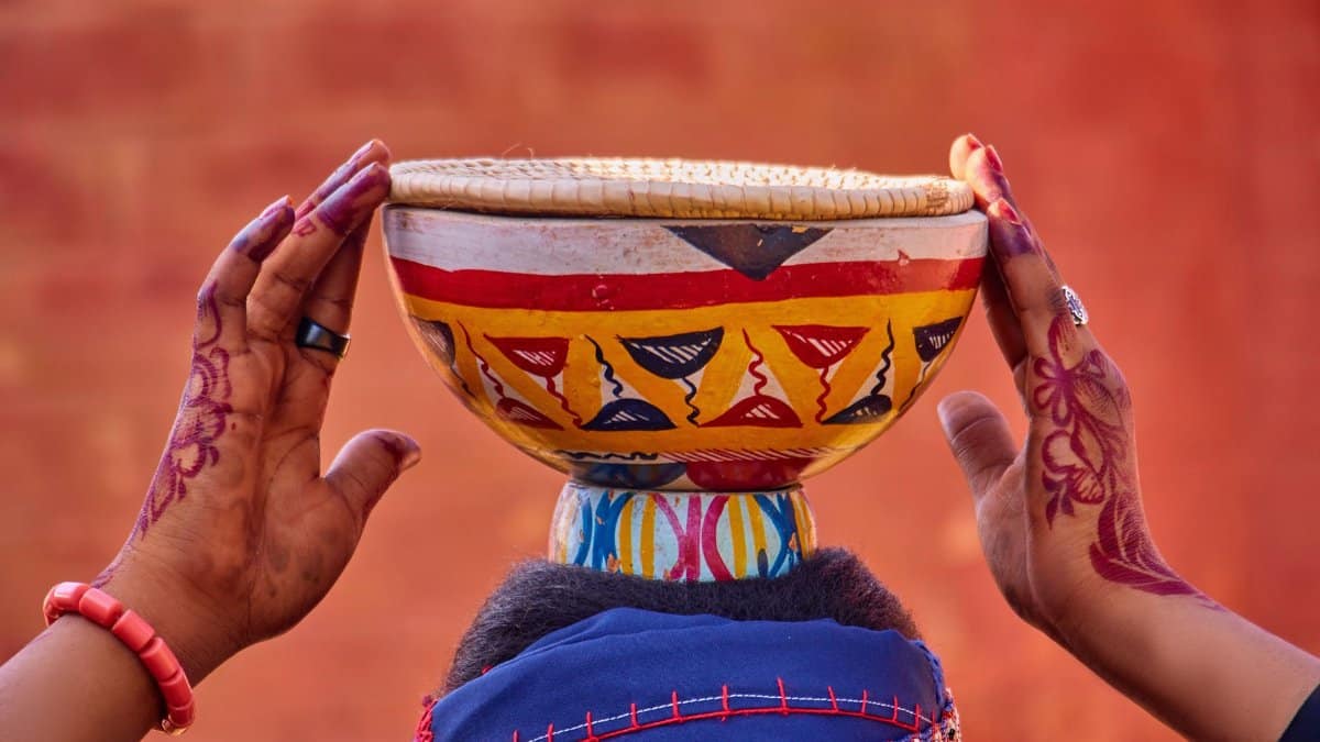 Traditional pot balancing on a woman's head with henna hand designs and vibrant colors.