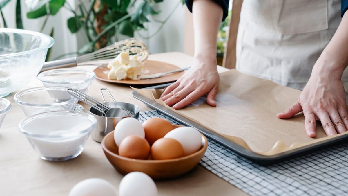 Hands preparing baking tray with ingredients ready for baking, including eggs and flour.