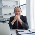 Smiling businessman in a suit with laptop and documents, exuding confidence.