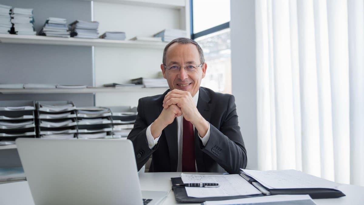 Smiling businessman in a suit with laptop and documents, exuding confidence.