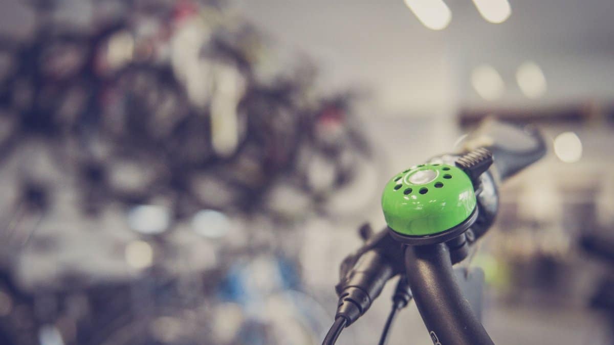 Close-up of a green bicycle bell on handlebars with blurred bike shop in background.