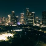 A stunning aerial view of Houston's illuminated skyline at night, showcasing skyscrapers and urban parks.