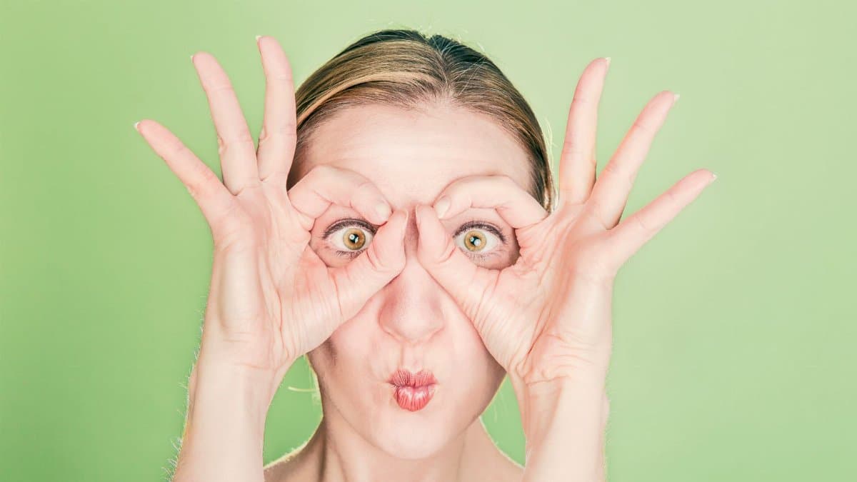 A woman creates a funny face with her hands and eyes against a green background. Perfect for whimsical themes.
