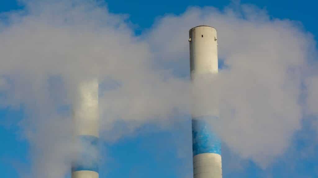 Twin industrial chimneys emitting smoke under a clear blue sky, highlighting air pollution concerns.