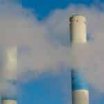 Twin industrial chimneys emitting smoke under a clear blue sky, highlighting air pollution concerns.