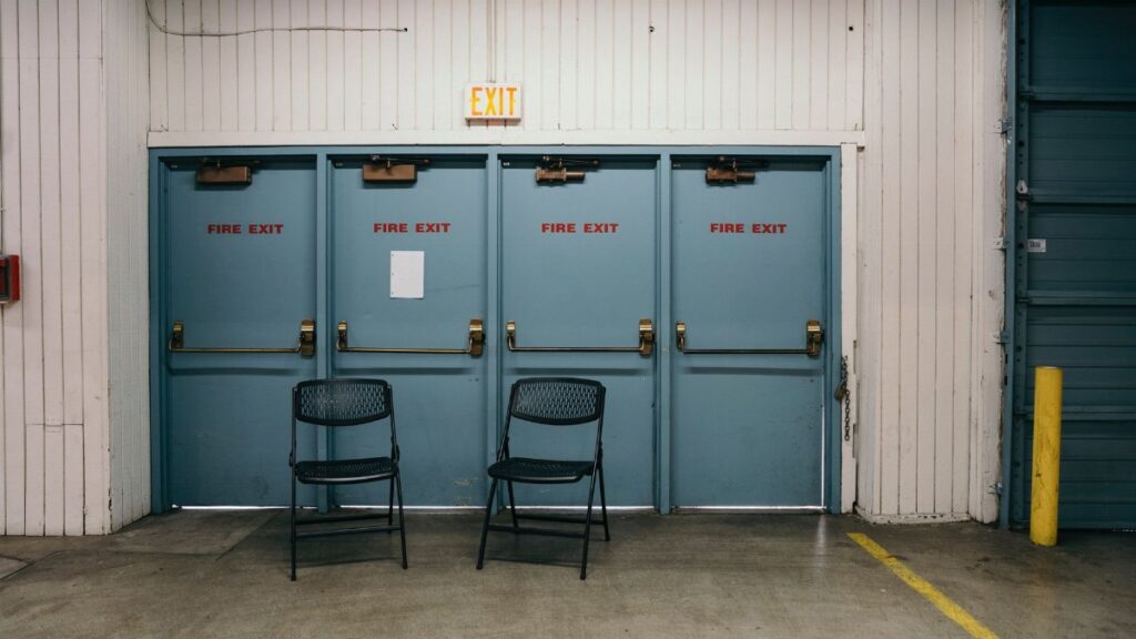 Industrial setting featuring three blue fire exit doors and two black chairs in a Portland warehouse.