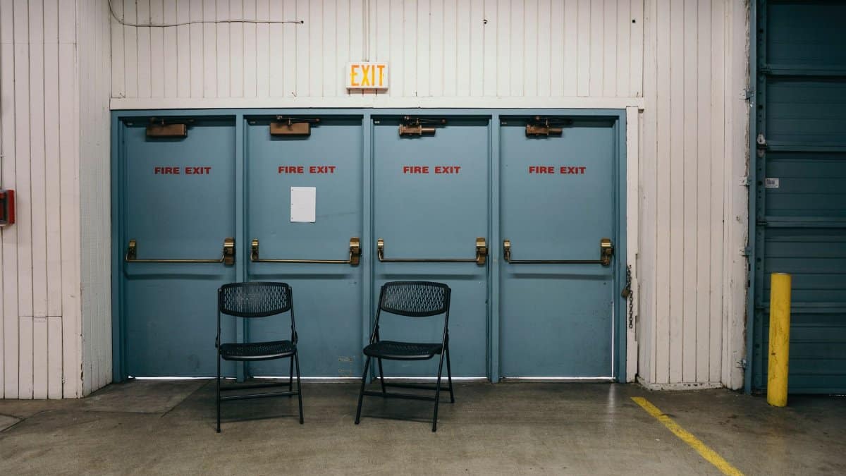 Industrial setting featuring three blue fire exit doors and two black chairs in a Portland warehouse.