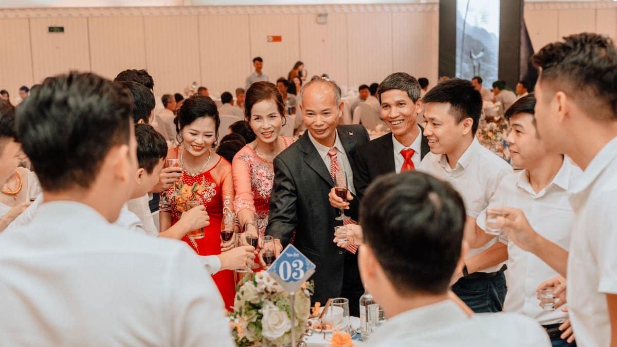 A joyous gathering at a wedding reception with people toasting and smiling indoors.