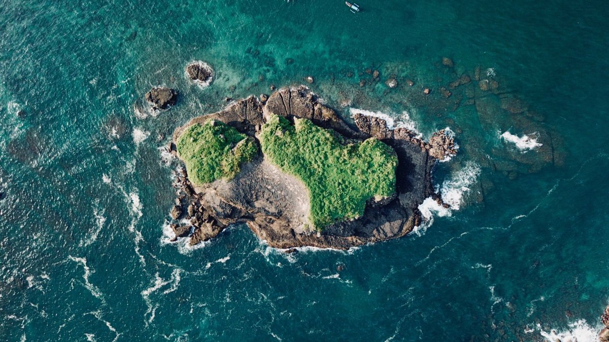 Discover the breathtaking aerial view of a tropical rocky island surrounded by turquoise ocean waves.