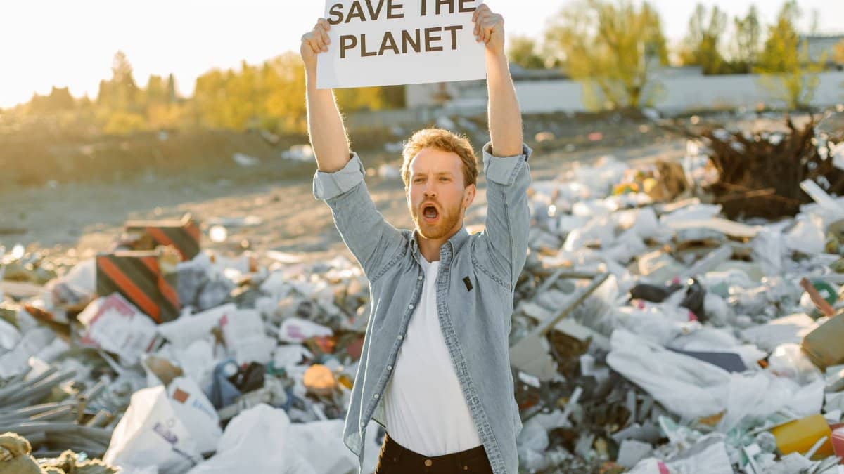 Passionate activist holding sign to save the planet at a landfill, promoting environmental awareness.
