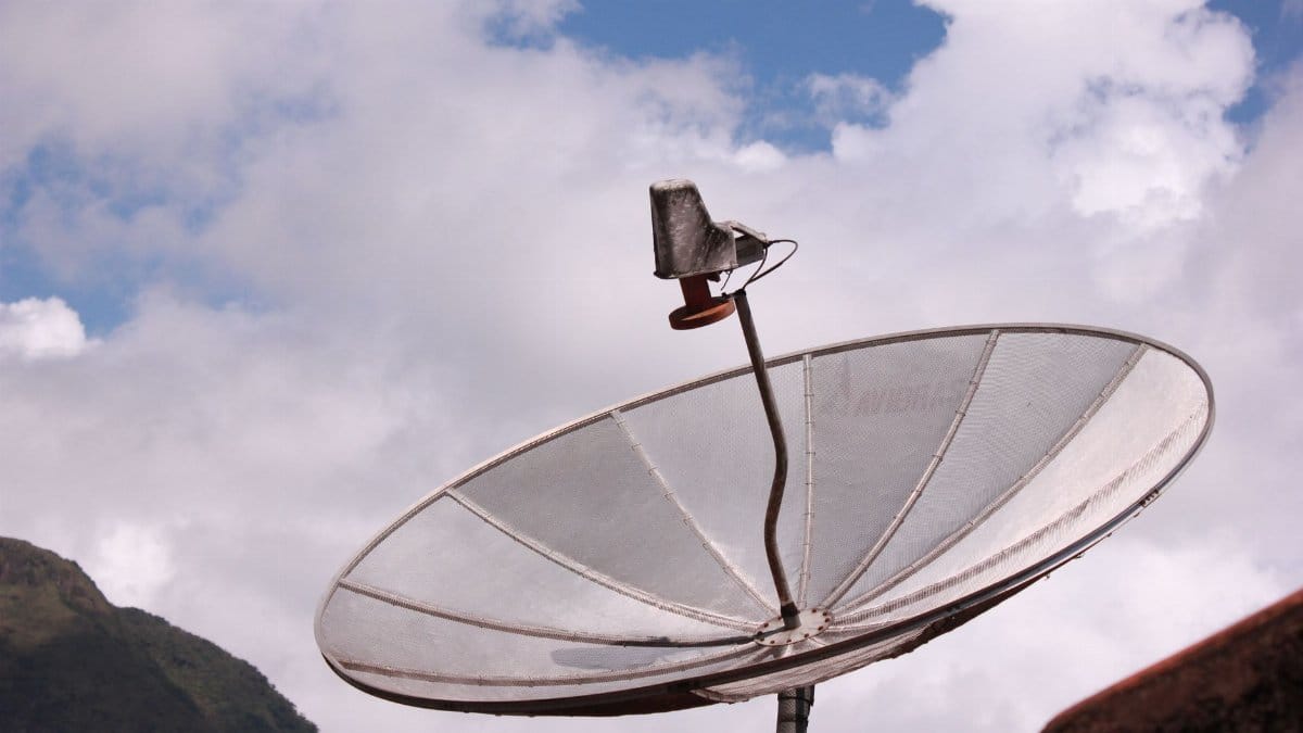 Silver satellite dish pointing skyward under a bright blue sky with scattered clouds.